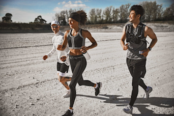 Three people running on a dirt track holding Huel products and smiling
