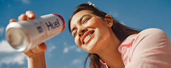 Woman drinking from a white and pink Huel Daily A-Z Vitamins energy drink can