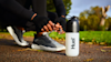 Man tying his trainers in a park ready to run, while next to a Huel shaker.