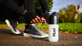 Man tying his trainers in a park ready to run, while next to a Huel shaker.