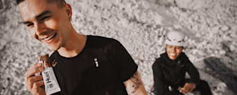 Man eating a chocolate Huel complete protein bar alongside a woman while on a hike