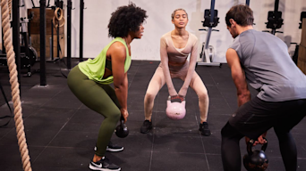 three people at the gym doing kettlebell squats