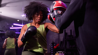 Woman doing boxing training on pads at a gym lit by purple neon lights