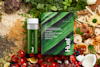 Huel Daily Greens pouch and bottle laying on a bed of different fruits and vegetables