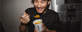 Image of a man smiling while eating from a pot of Huel Hot & Savoury vegan instant meal