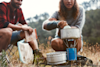 man and woman cooking in a pot on a camping stove outside