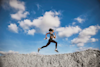 Woman running on top of a mountain holding a Huel shaker and with clouds in the background