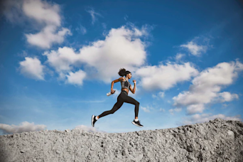Woman running on top of a mountain holding a Huel shaker and with clouds in the background