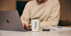 person sat at desk using their laptop with a Huel Hot and Savoury pot in front of them