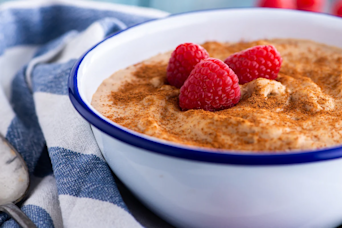 a bowl of porridge with powdered cinnamon and raspberries on top
