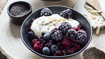 A bowl with blackberries, blueberries, raspberries, and redberries, with yoghurt and chia seeds on top