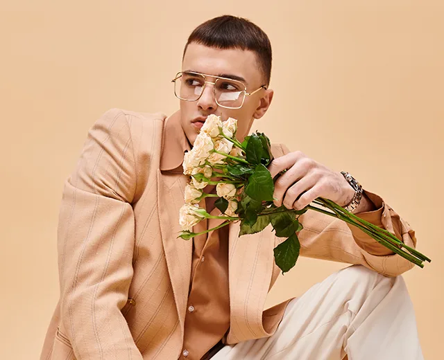 Istuva silmälasipäinen henkilö kädessään kukkia