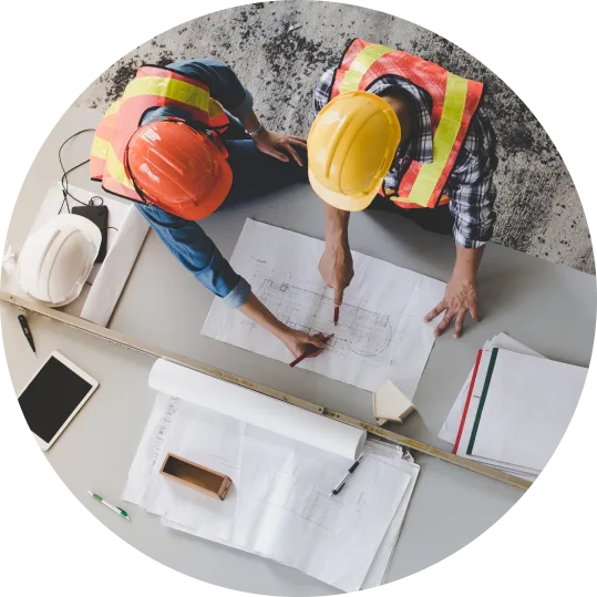 Two people wearing safety helmets looking over construction documents.