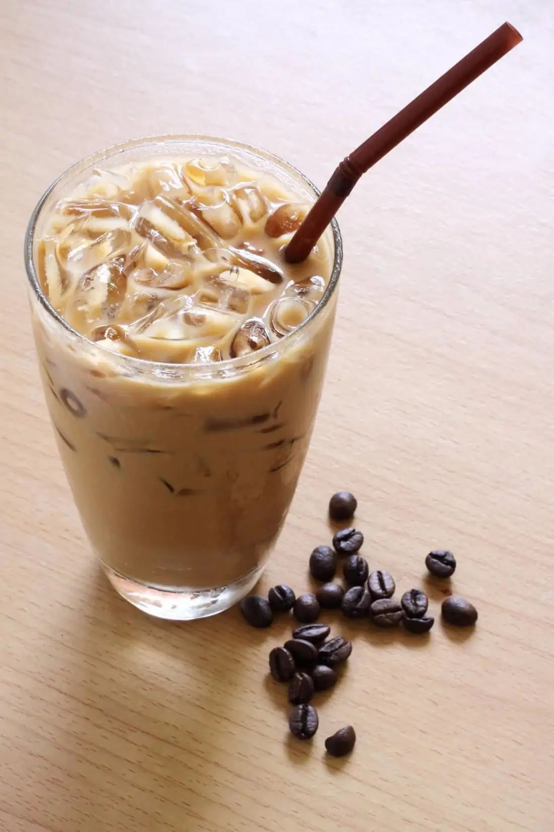 An image of a glass containing a drink with iced coffee, with some coffee beans beside it