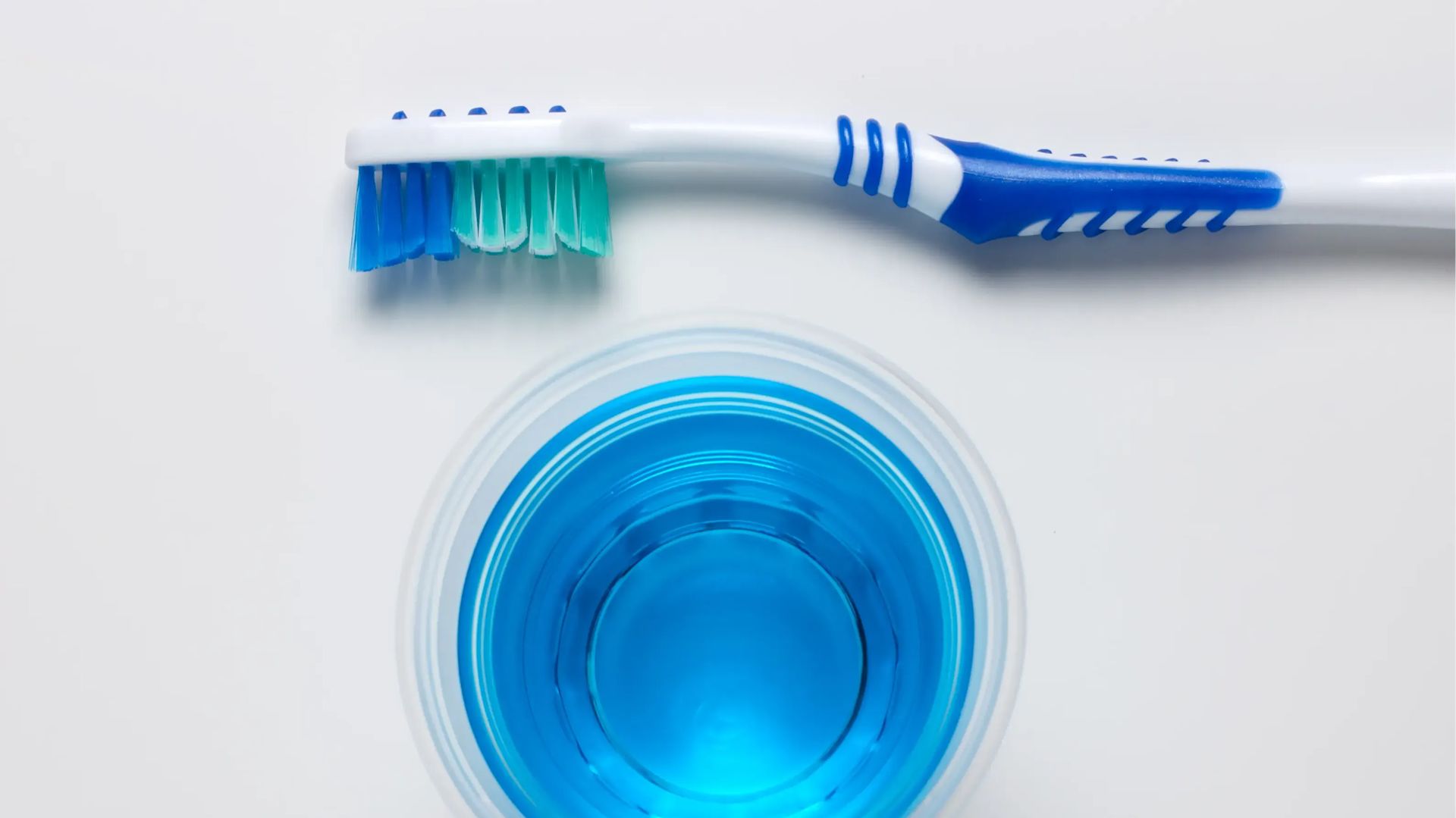 Oben und unten jeweils eine Zahnbürste und in der Mitte ein blaues Mundwasser.