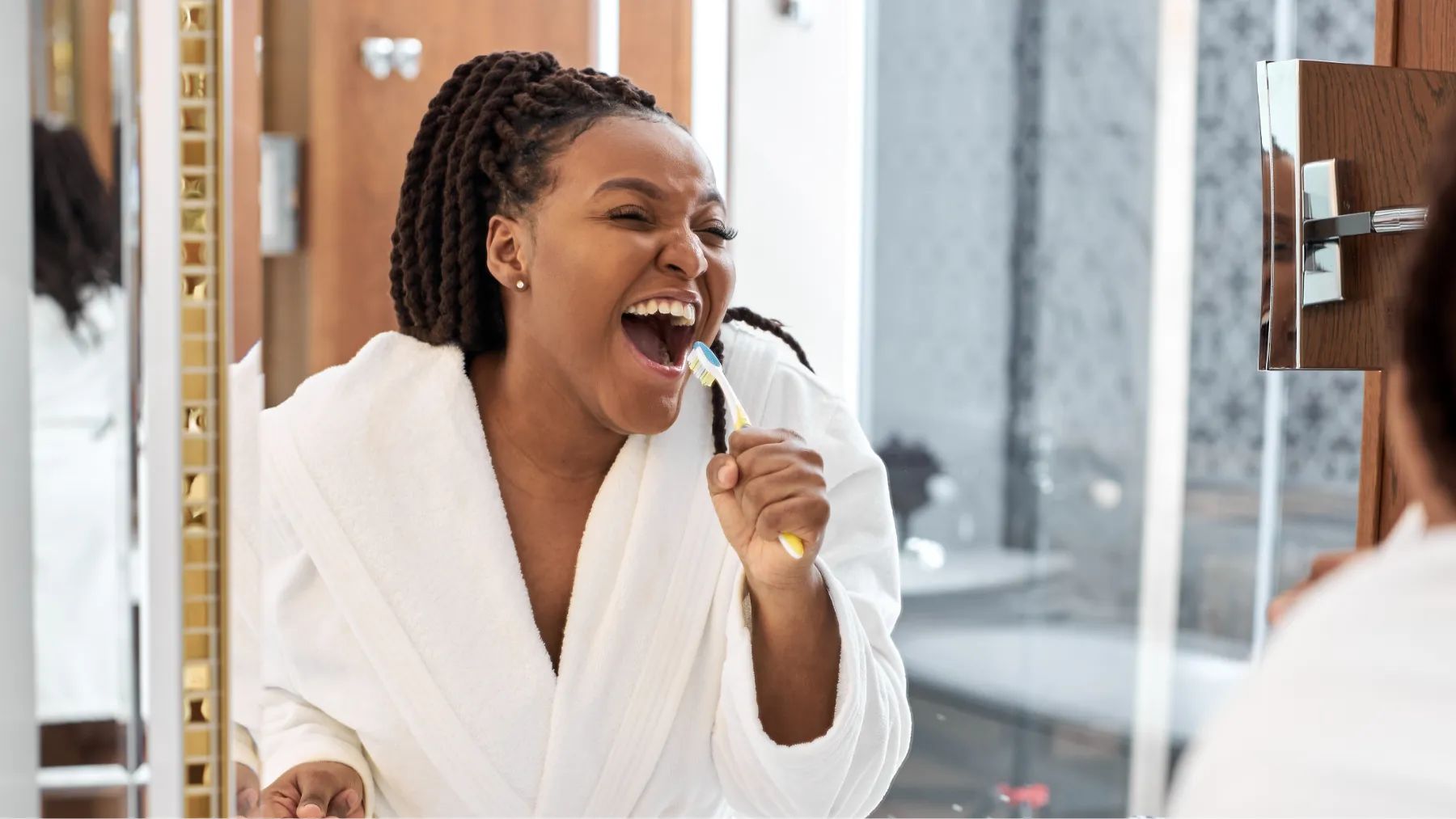 A woman singing in front of the mirror using her toothbrush as if it were a microphone