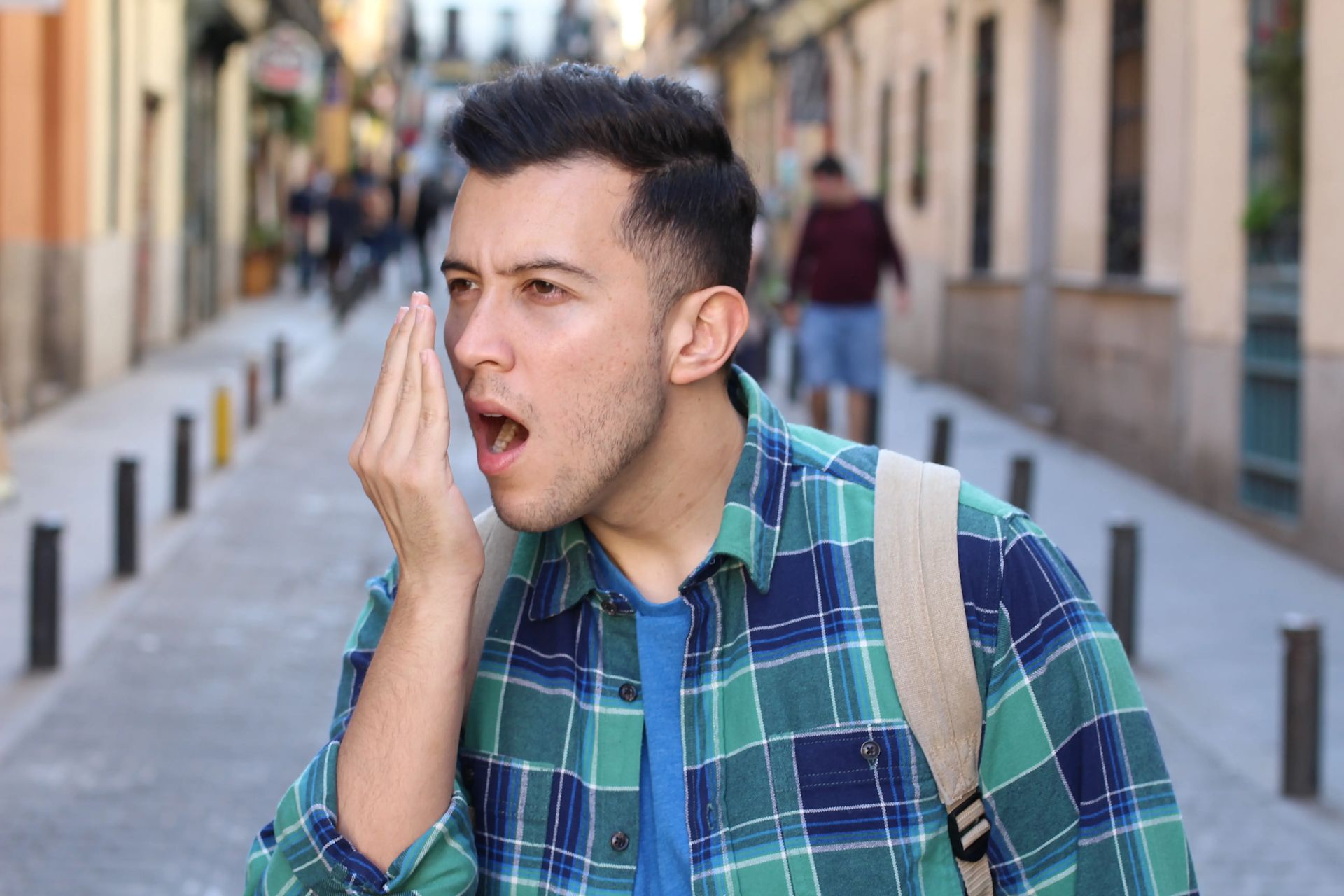 Un homme tenant sa main devant sa bouche et soufflant dedans.