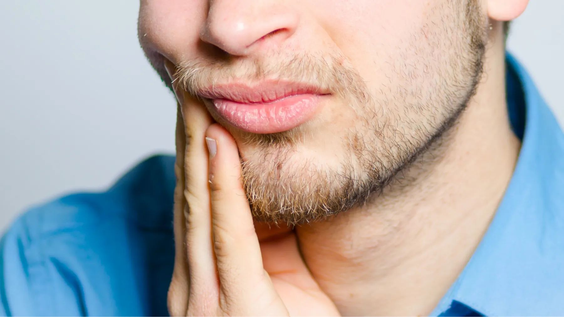 A man touches his cheek, showing a moment of tooth and cavity related pain