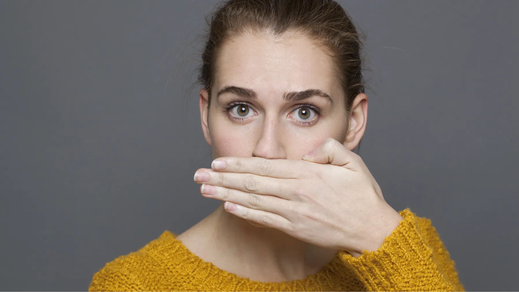 A woman covers her mouth with her hand, representating a moment of prevent and treat bad breath