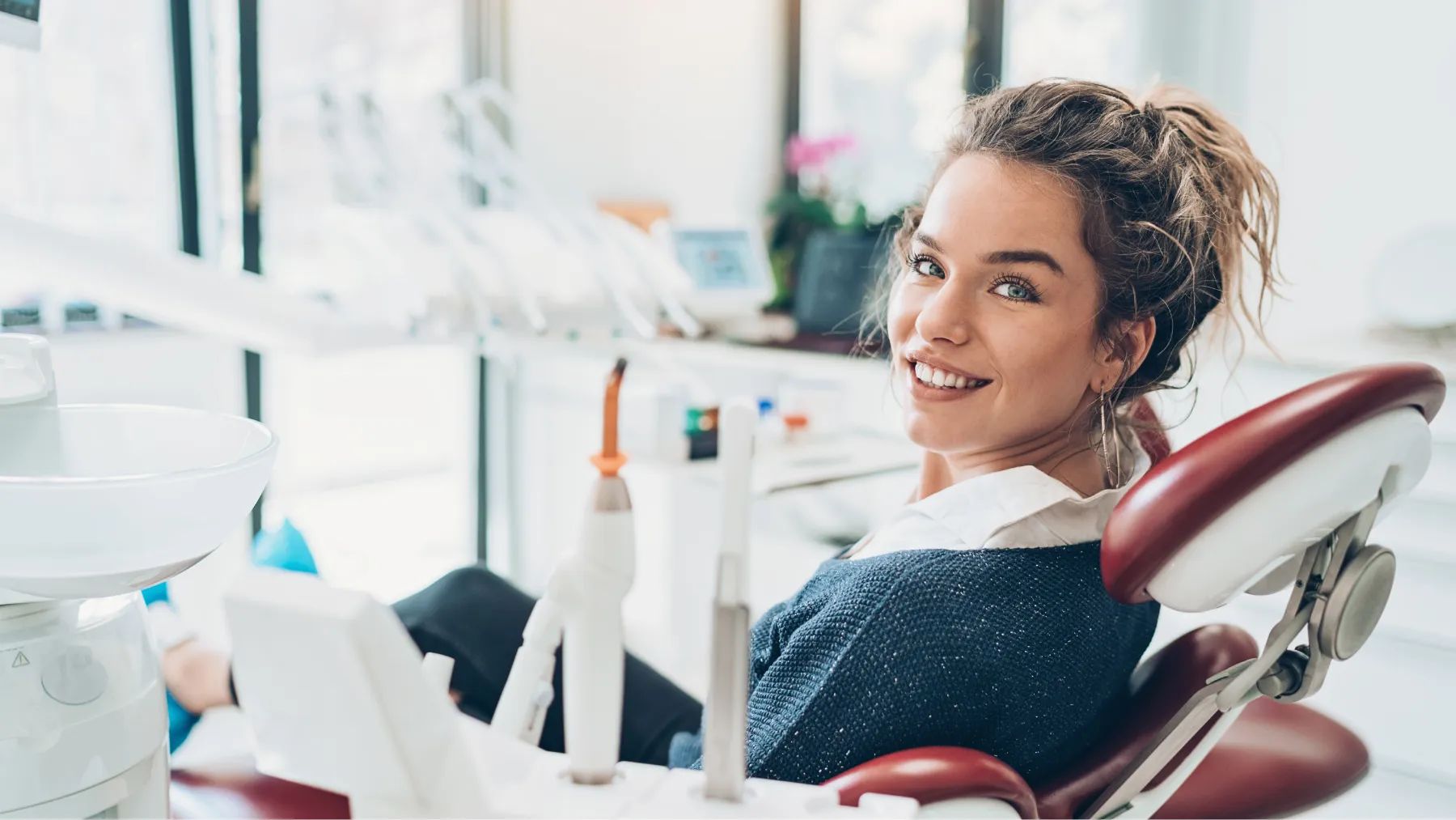 A smiling woman seated in a dental chair, preparing for a dental examination or treatment