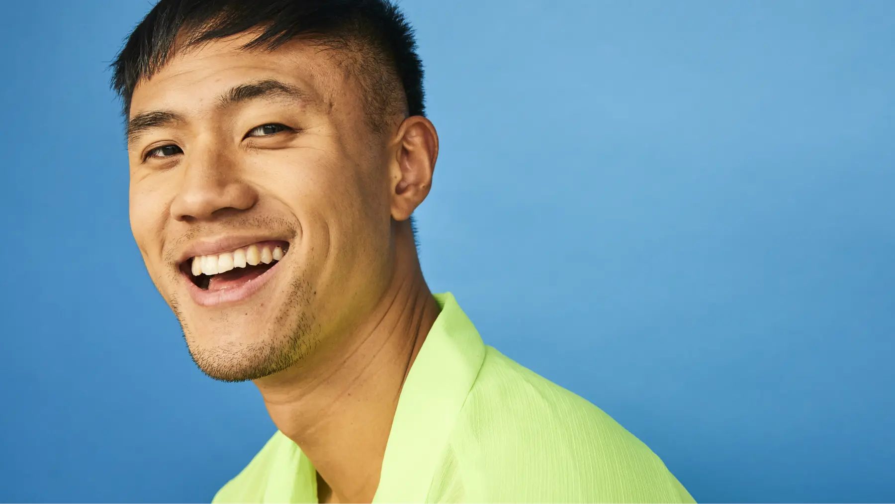 A smiling man dressed in a vibrant green shirt poses for the photo, hero for stop the grind article