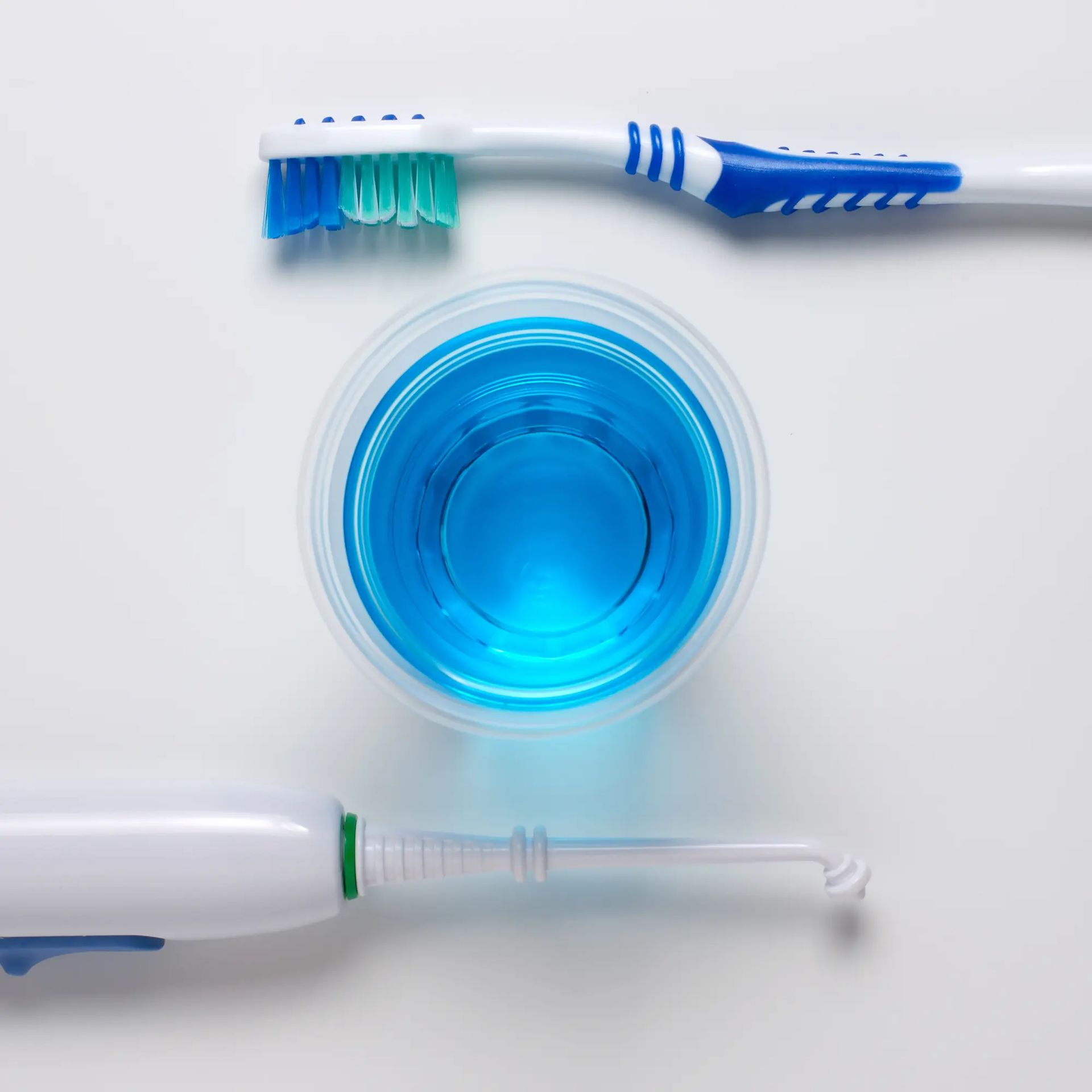 Oben und unten jeweils eine Zahnbürste und in der Mitte ein blaues Mundwasser.