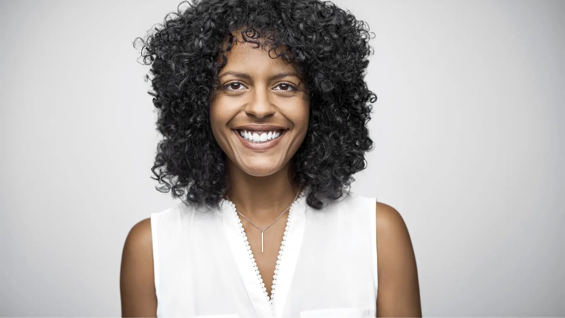 A smiling woman with curly hair looks intently ahead in a cozy environment