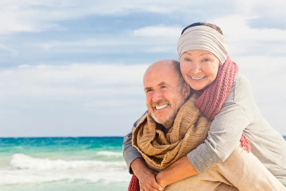Älterer Mann mit gesunden Zähnen ist am Meer mit seiner Frau und lächelt sympathisch