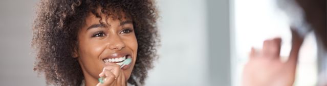 A young woman looking at the mirror and brushing her teeth.