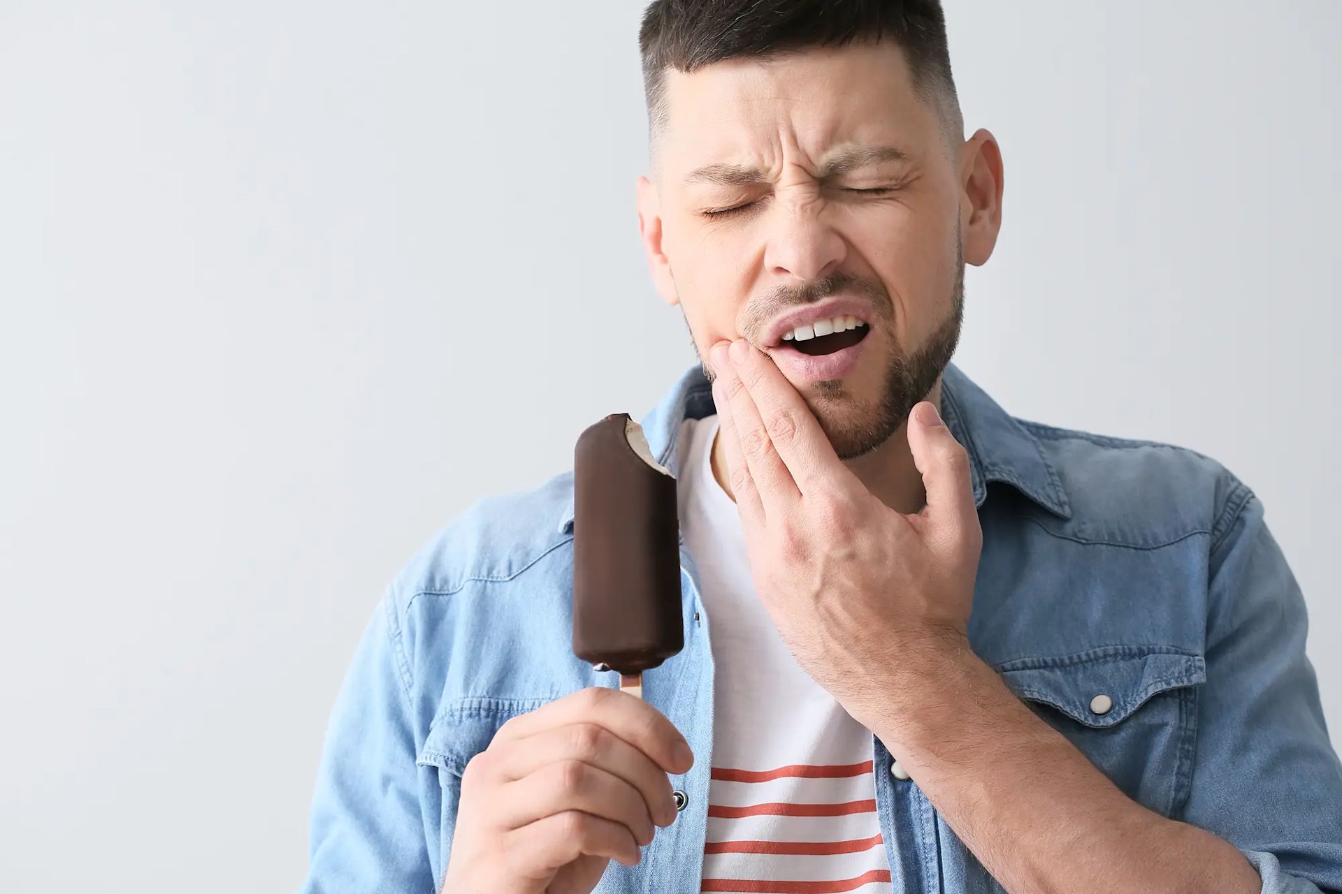 Ein Mann, der ein Eis in den Händen hält und dabei schmerzvoll schaut und seine Hände an der Wange hat.