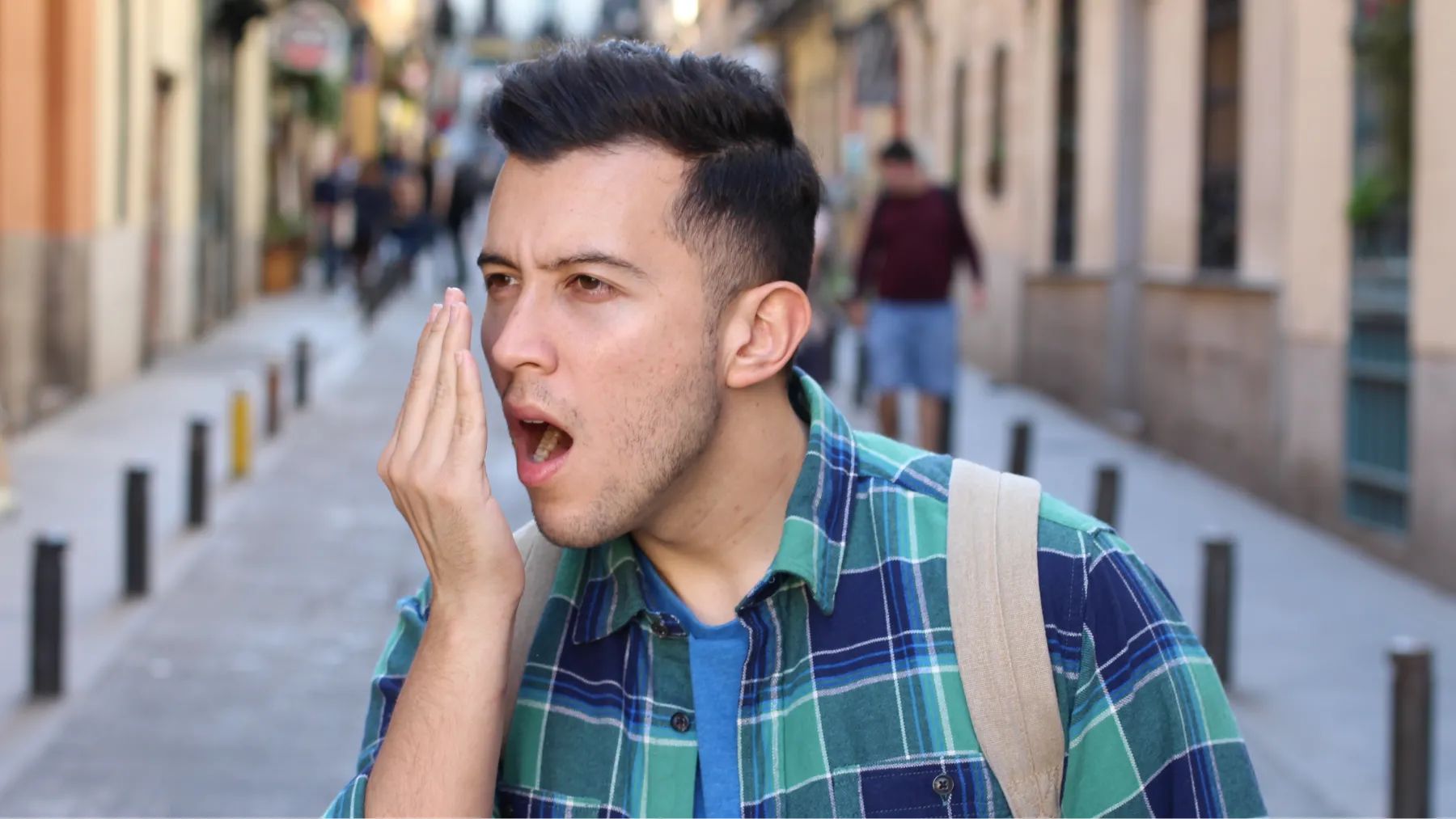 A man breathes into his hand, showing a moment of concern about signs of bad breath