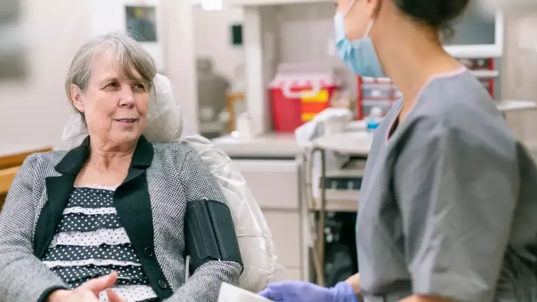 A dentist speaks with a woman wearing a hospital gown clarifying about diabetes and oral health