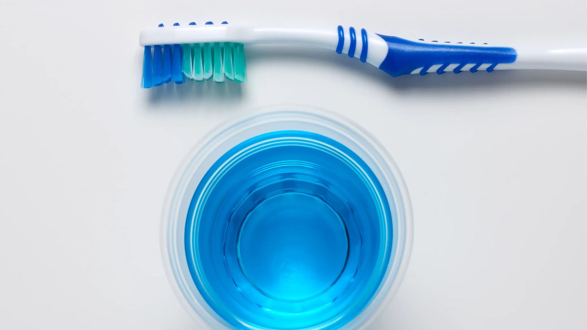 Oben und unten jeweils eine Zahnbürste und in der Mitte ein blaues Mundwasser.