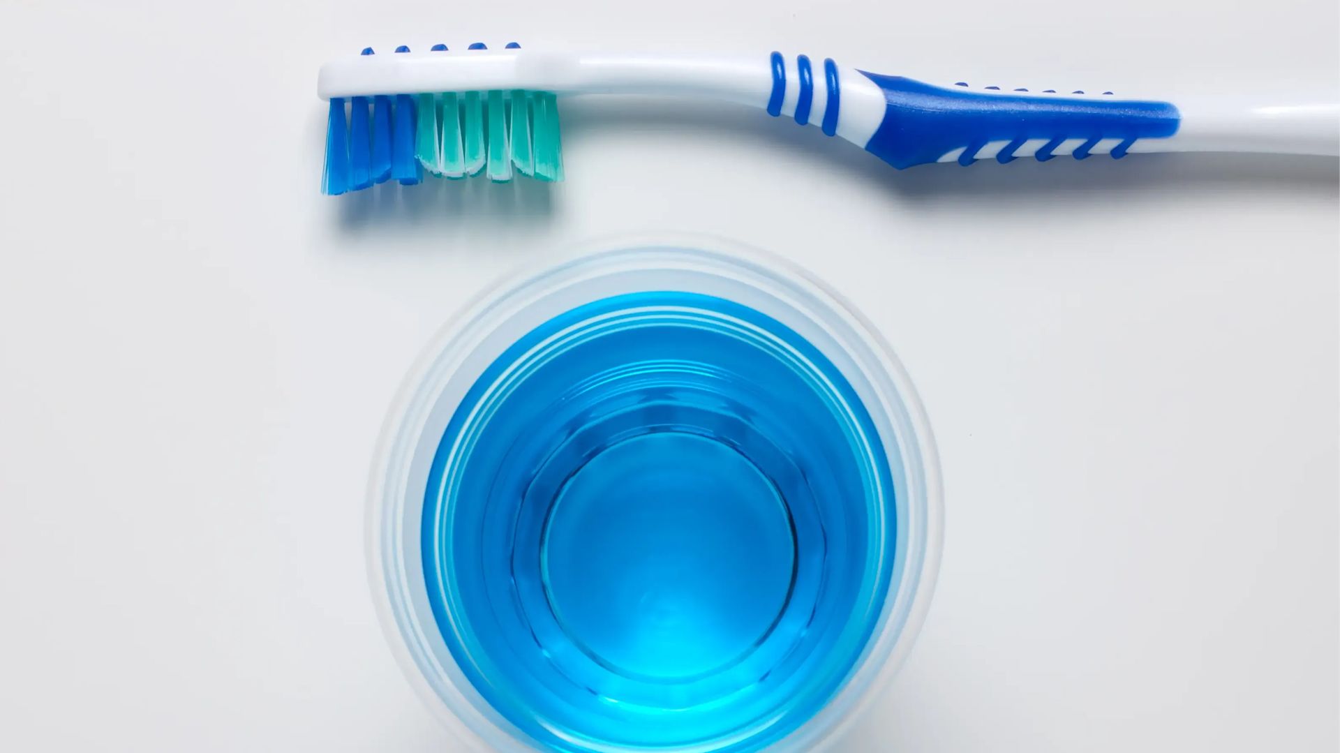 En haut et en bas une brosse à dents, et au centre un bain de bouche bleu.
