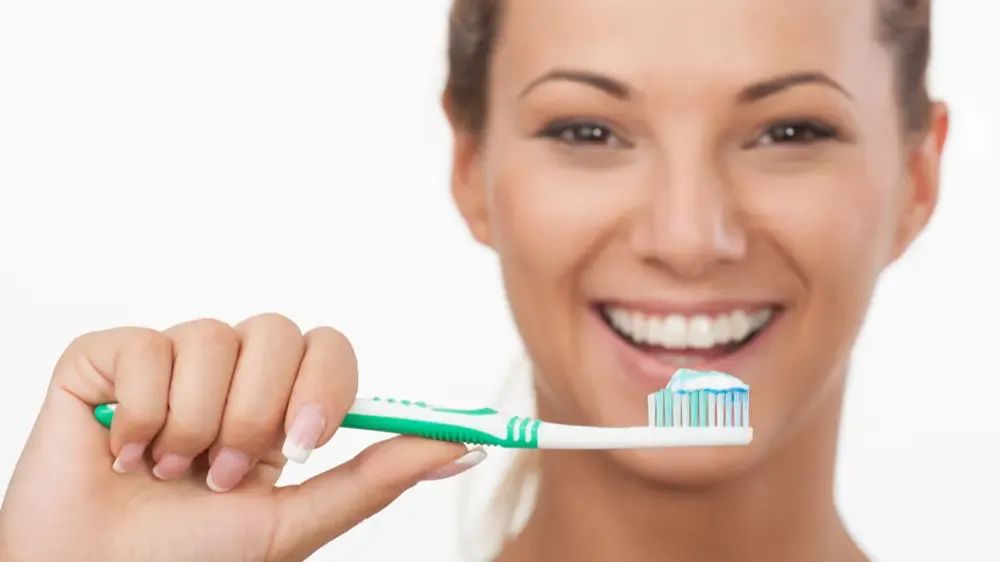 Une femme souriante, la bouche ouverte, tenant une brosse à dents avec du dentifrice.