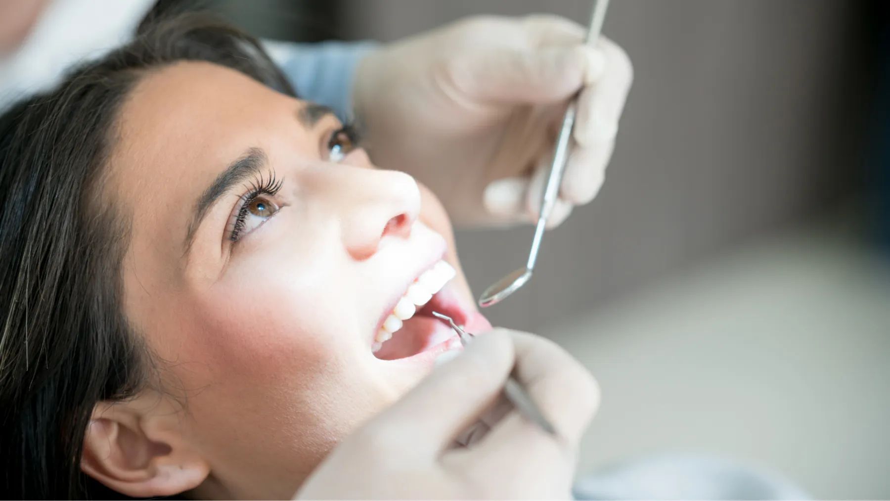 A woman sits in a dental chair while a dentist examines her teeth with a dental tool