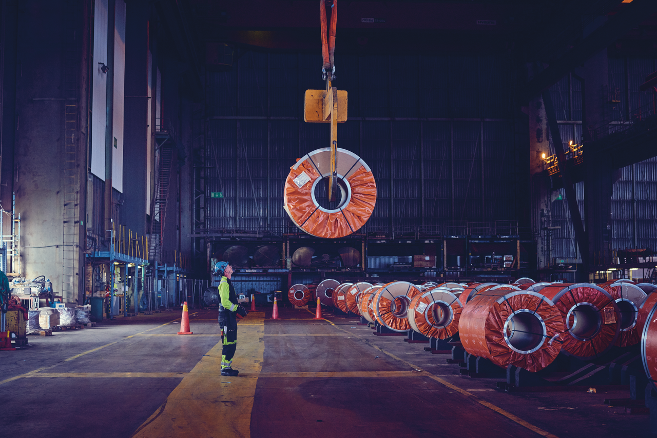Photo of a DFDS employee standing below a steel coil that is being lifted inside a warehouse 
