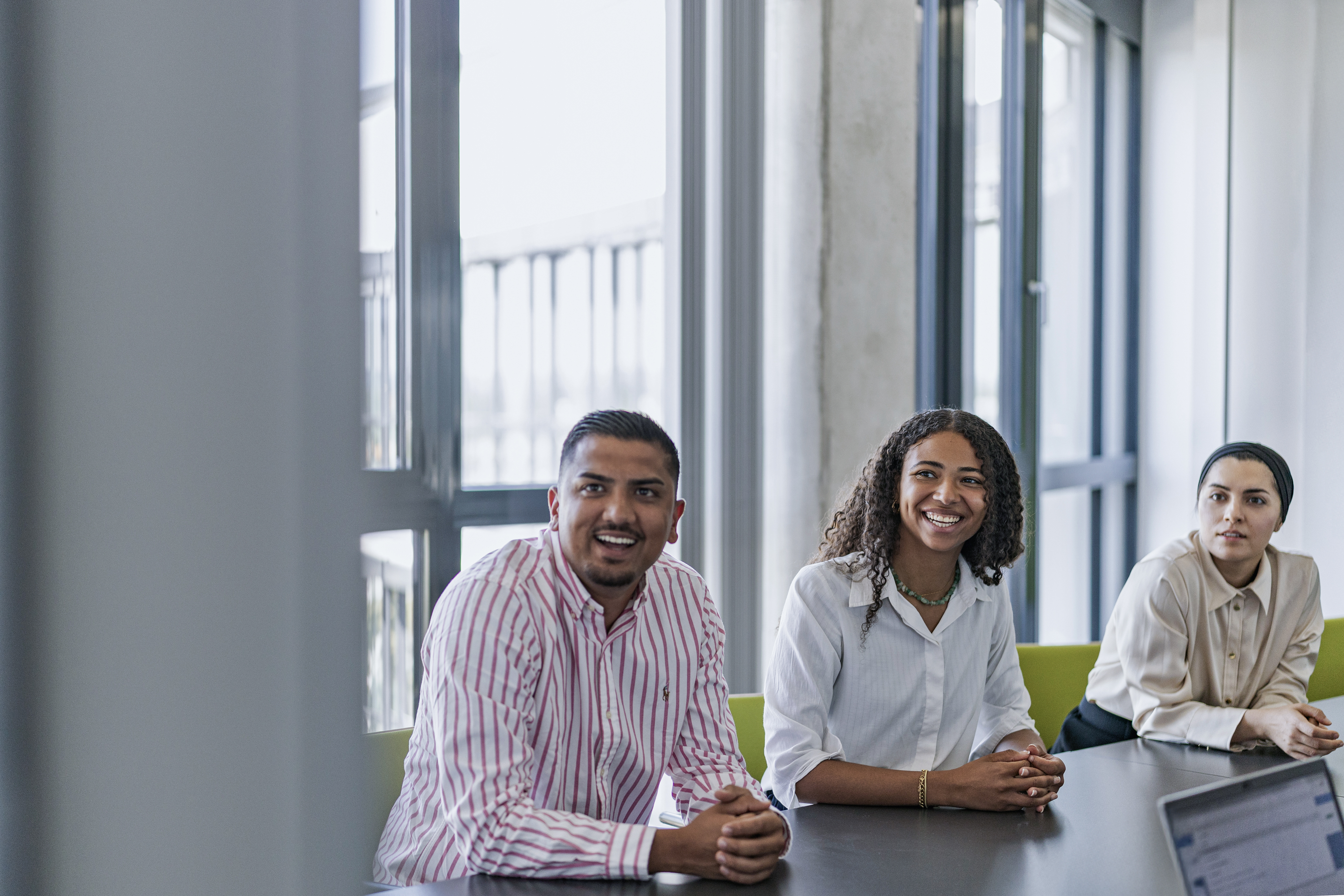 Ein Mann und zwei Frauen im Meetingraum lachend