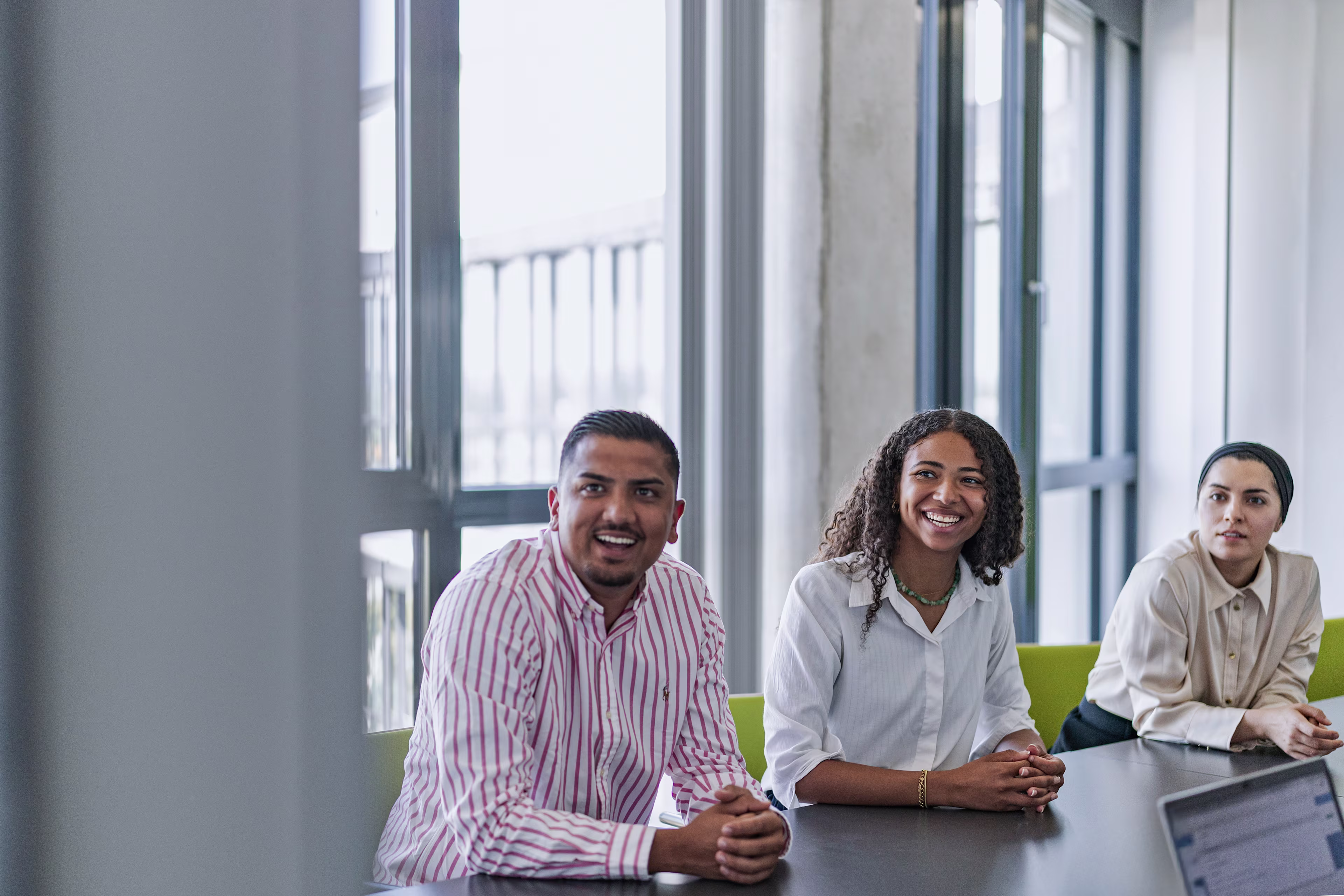 Ein Mann und zwei Frauen im Meetingraum lachend