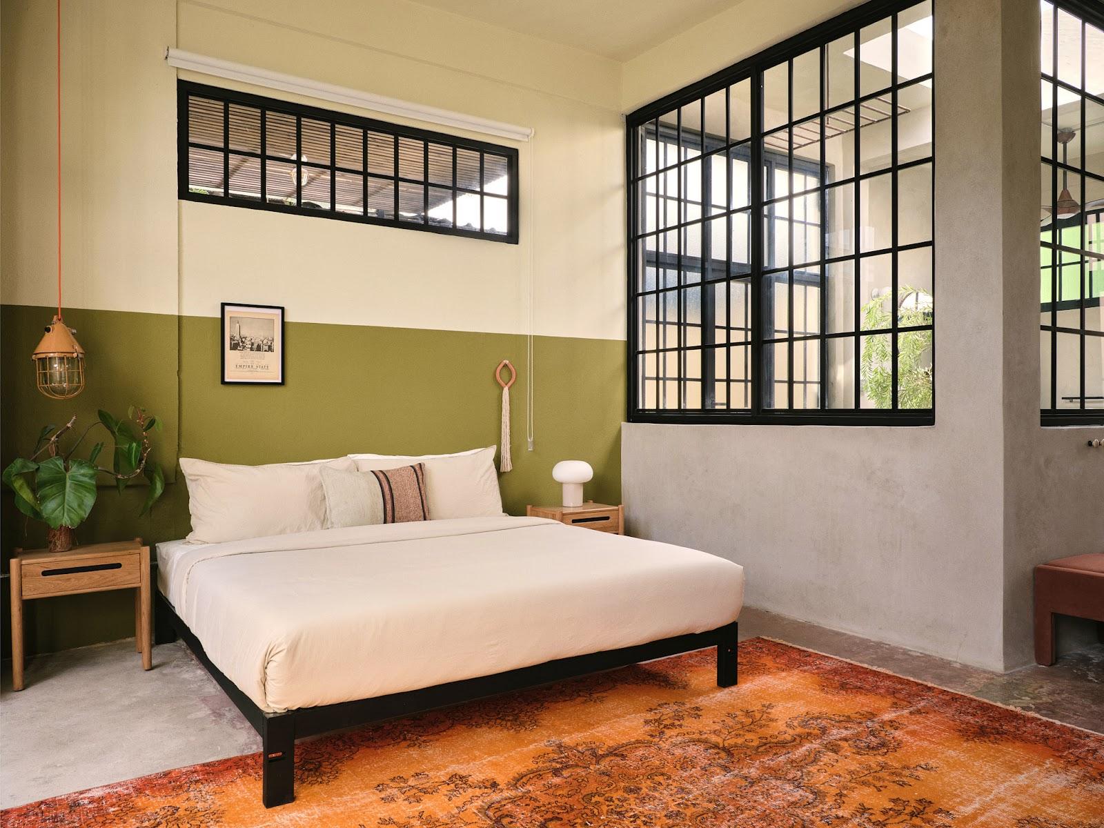 A loft studio bedroom at Paz by DW, a Dreamers Welcome stay in San Juan, with olive-green walls and tall industrial windows.