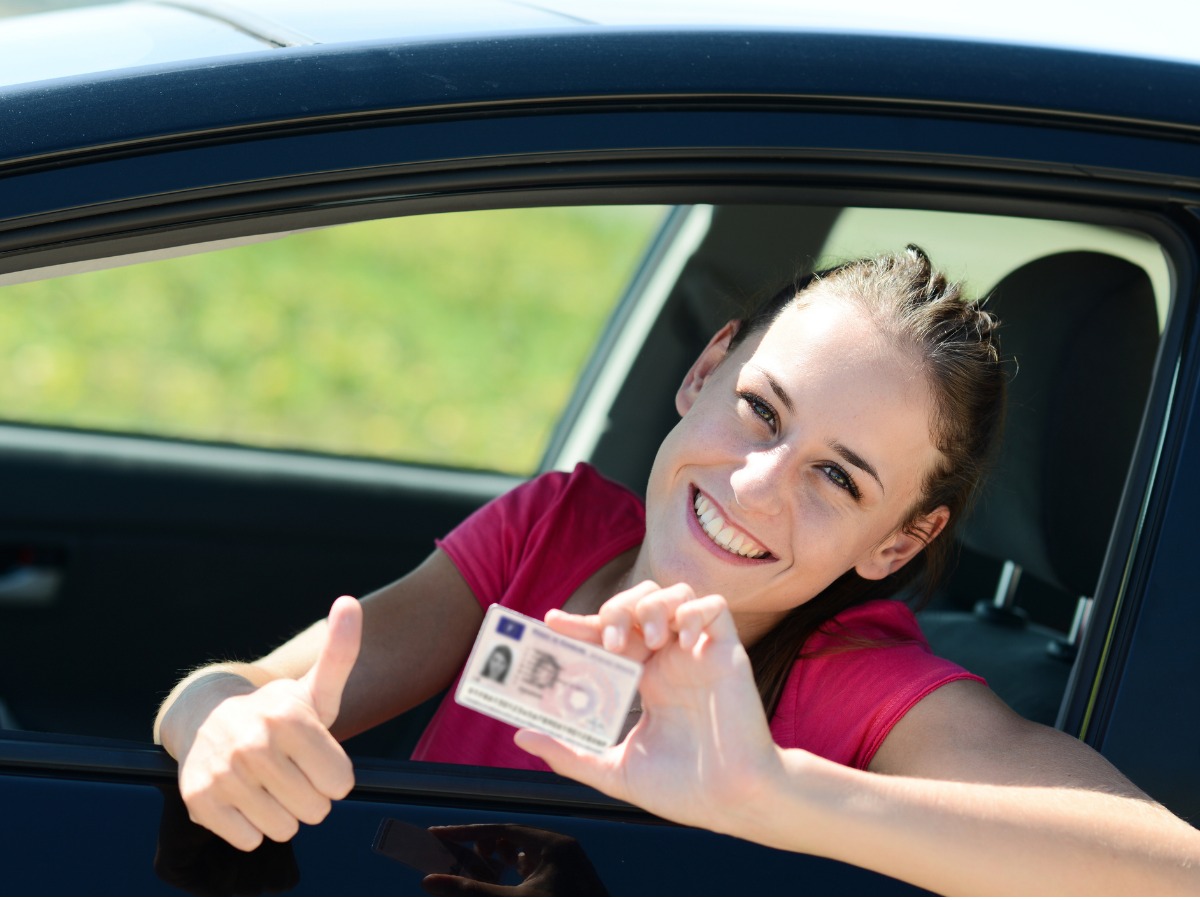 cheerful-happy-young-woman-in-car-showing-new-driving-license-picture-id492415362