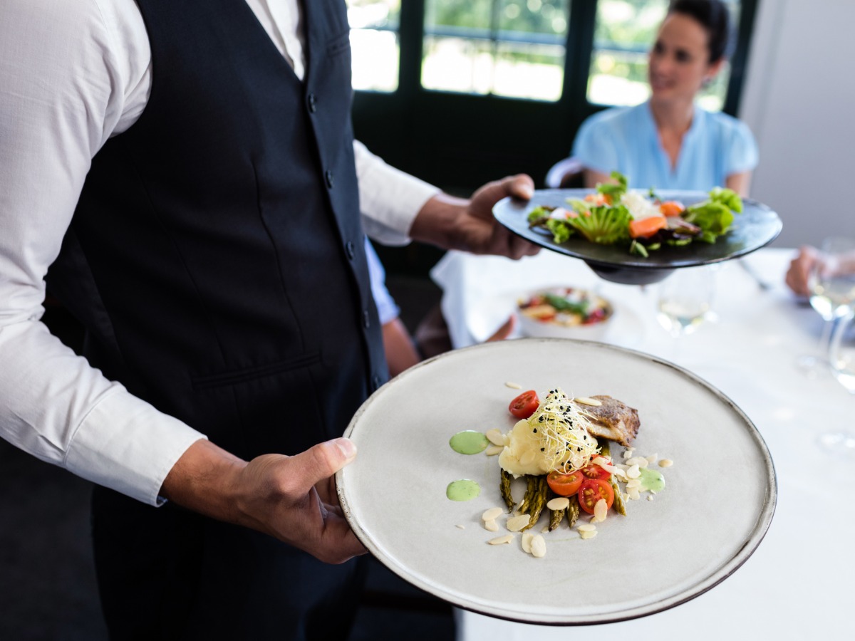 portrait-of-waiter-standing-with-meal-next-to-customers-picture-id698759452