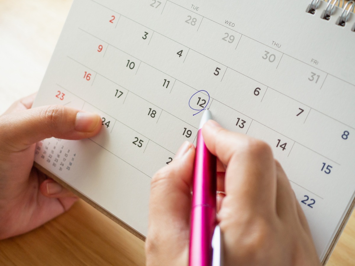 calendar-page-with-female-hand-holding-pen-on-desk-table-picture-id1061085192