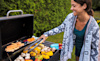 A young woman uses tongs to turn a colourful array of vegetables cooking on an outdoor barbecue
