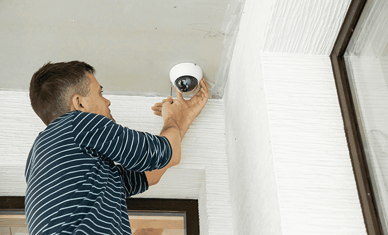 Man installing a security camera on the ceiling of his front porch just near the front door