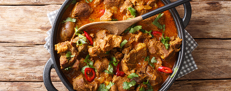 A pan of beef curry with red chilli and a wooden spoon