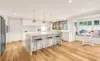Bright open plan kitchen with black stools timber floors and a trio of brasslook pendant lights above a white kitchen island