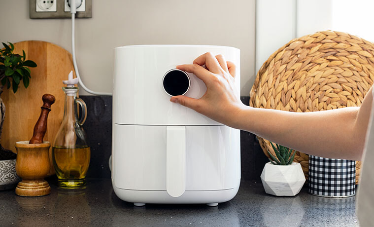 A hand adjusting a black dial on a white air fryer next to power point