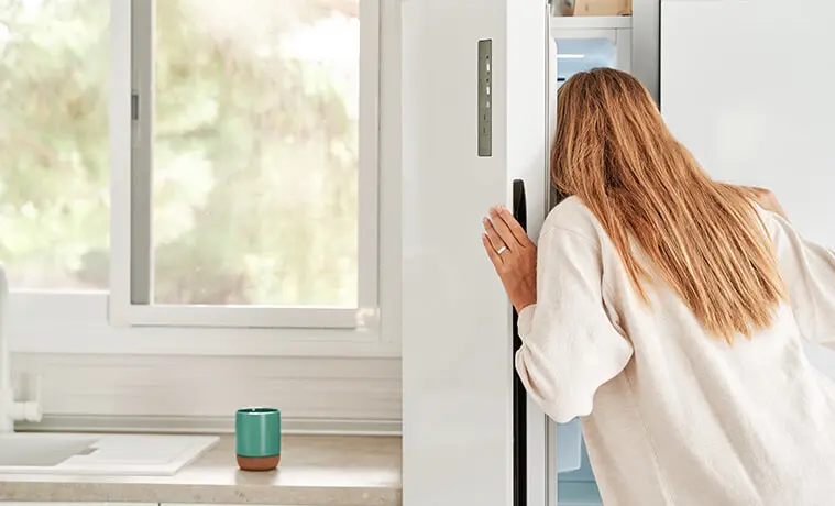Rear view of a woman looking behind the door of her upright freezer to see whats inside