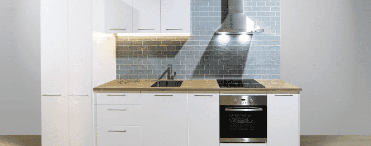 A white flat pack kitchen with blue splashback tile and a timber countertop